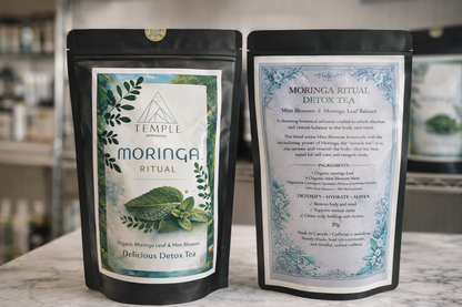 Two packages of Temple Moringa Ritual Detox Tea on a wooden surface with a blurred background.