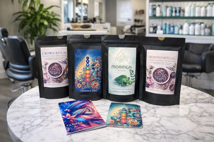 Four packages of 'The Temple' brand tea on a marble table with colorful cards in a salon setting.